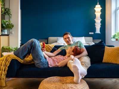 Family couple man woman making selfie on smartphone looking at screen sitting and lying on couch in modern apartment. Happy wife and husband photographing on phone laughing and smiling. Rest relax.
